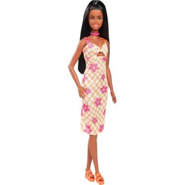 Imagem de Barbie Fashionistas boneca número 233 com cabelo preto, que usa um vestido xadrez a meia perna em tons de laranja e flor rosa com colar e sandálias, HYT91