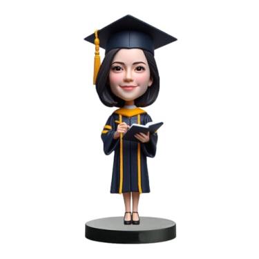 Imagem de Bobblehead de graduação em vestido com detalhes dourados segurando caderno e caneta feitos à mão personalizados a partir de sua foto, perfeito para espaços acadêmicos para graduados abraçando o